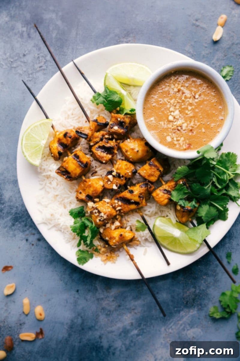 Grilled peanut butter chicken skewers beautifully arranged on a plate, with a small bowl of rich peanut sauce on the side and fresh cilantro for garnish.