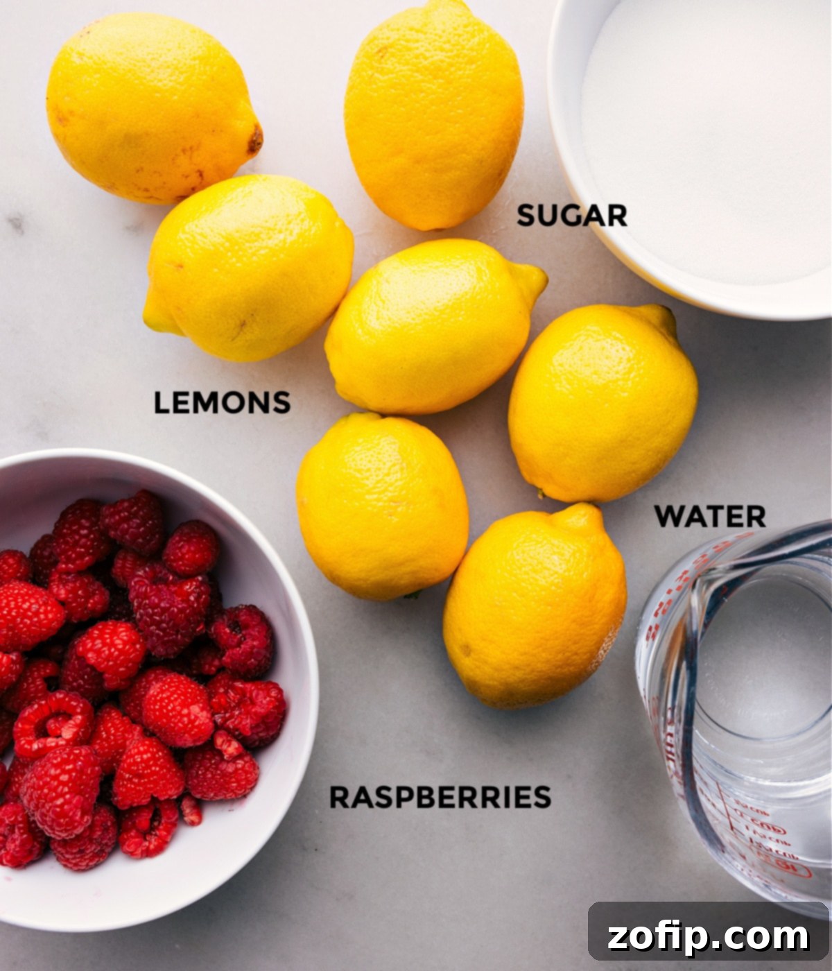 Ingredients for Homemade Raspberry Lemonade Fresh ingredients laid out: whole lemons, a bowl of bright red raspberries, granulated sugar, and a glass of water, ready for making lemonade.