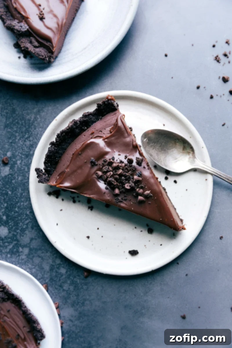 A perfectly sliced chocolate tart adorned with delicate Oreo crumbs, showcasing its multiple indulgent layers, ready to be enjoyed.