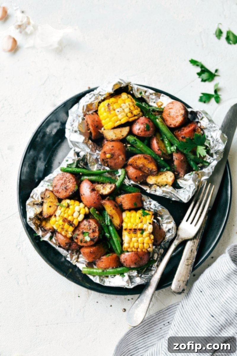 Overhead image of two garlic butter sausage and veggies in foil packs, ready to be cooked or served.