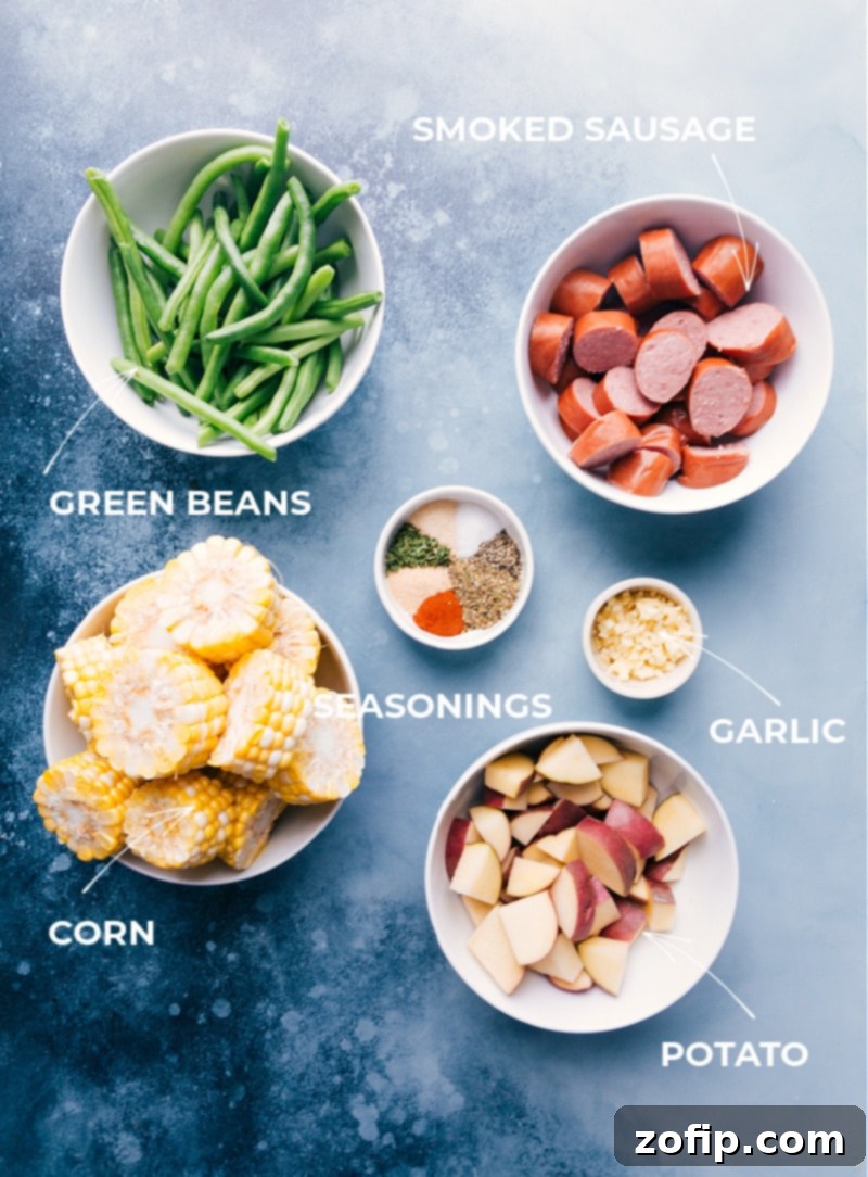 A vibrant display of fresh ingredients for garlic butter sausage and veggies foil packs, including corn, potatoes, green beans, and smoked sausage.