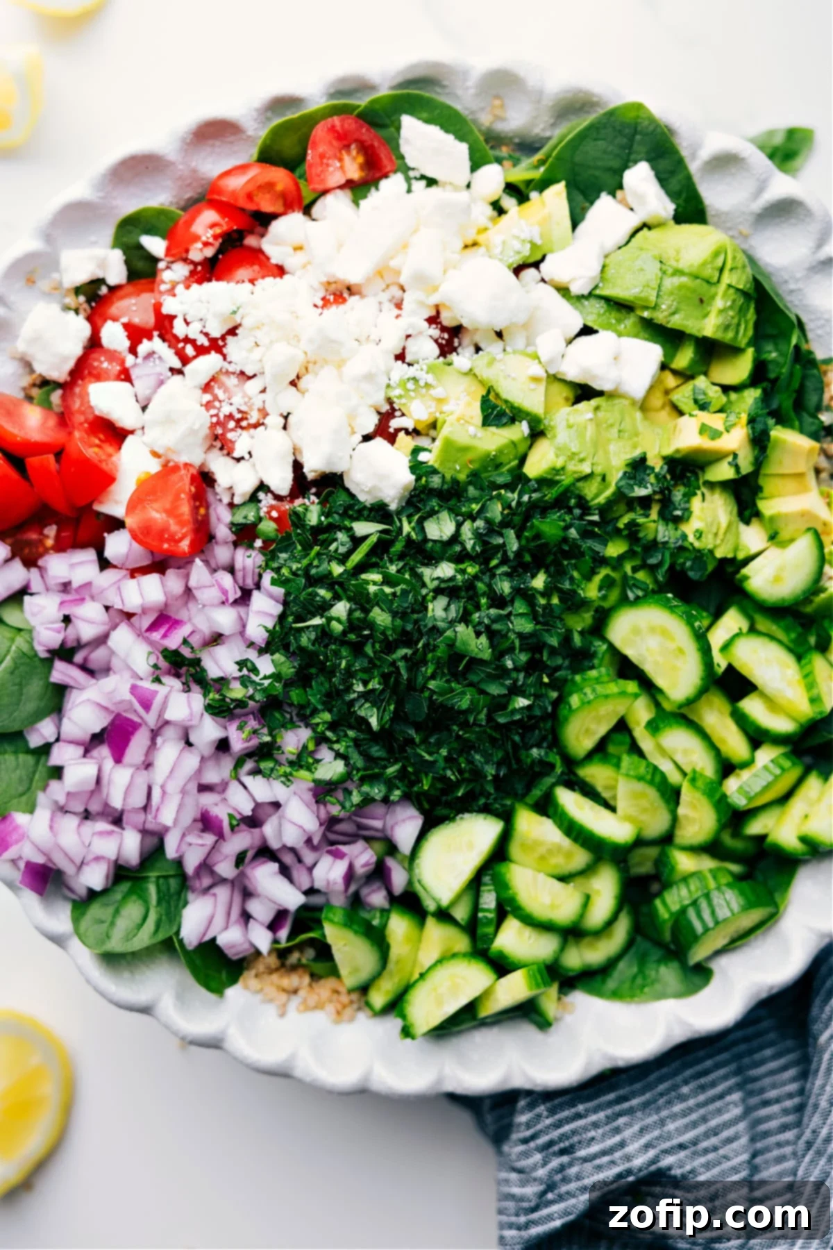 All the components of the quinoa salad, including dressing, quinoa, and chopped vegetables, laid out and ready for mixing.