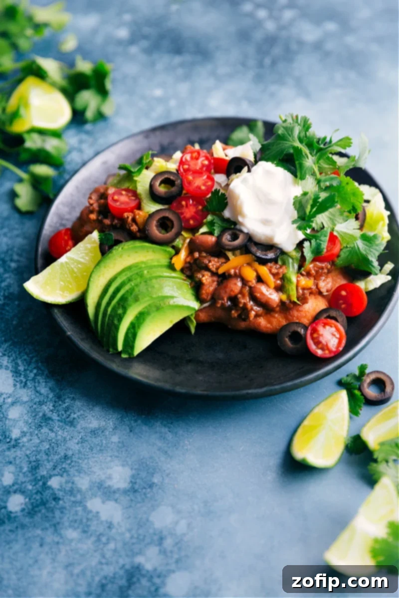 Delicious Navajo Tacos featuring homemade Fry Bread, seasoned beef, beans, and fresh toppings. A vibrant plate of Navajo Tacos, showcasing the golden Fry Bread beneath a generous mound of seasoned beef, beans, cheese, lettuce, and tomatoes.