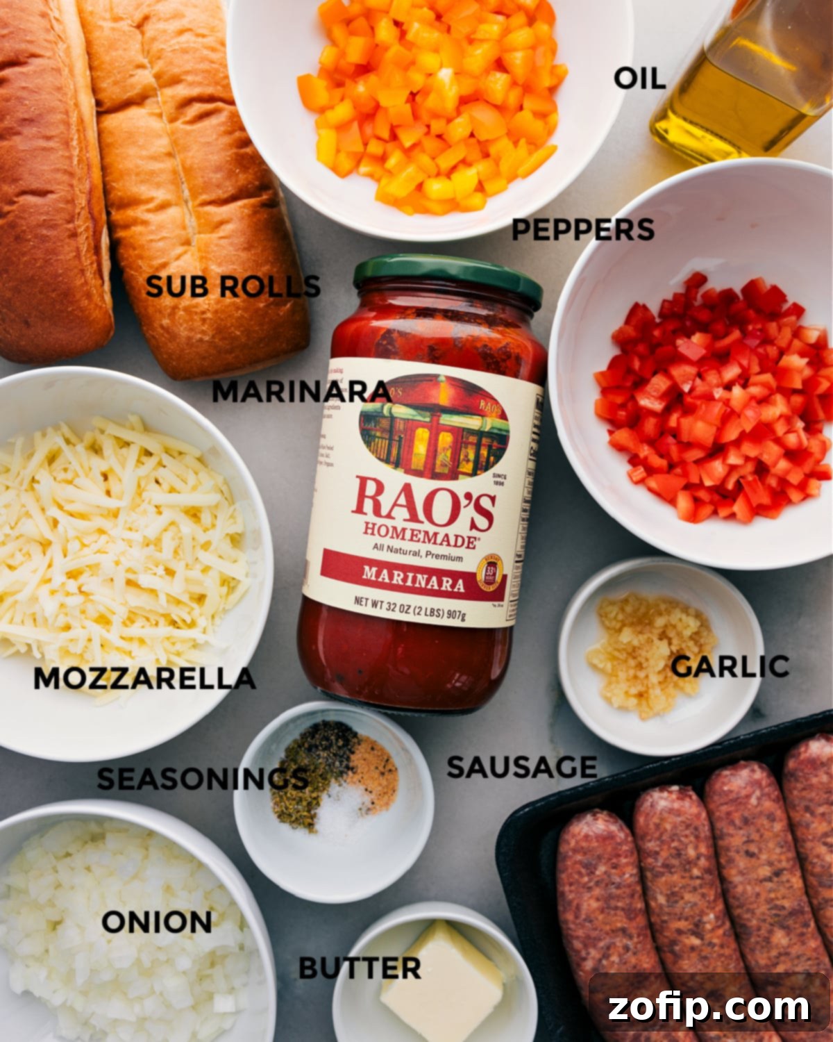 A vibrant selection of ingredients laid out for easy assembly, including colorful bell peppers, fresh hoagie rolls, a jar of marinara, shredded mozzarella, diced onion, a stick of butter, Italian sausage, minced garlic, and various seasonings.