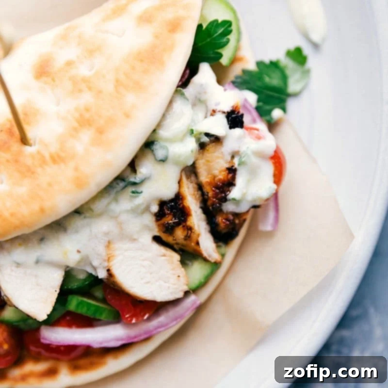 A complete and generously filled chicken gyro, showcasing layers of perfectly grilled chicken, crisp vegetables, and a creamy tzatziki sauce, all perfectly wrapped in a soft pita and presented on a plate, ready to be devoured.