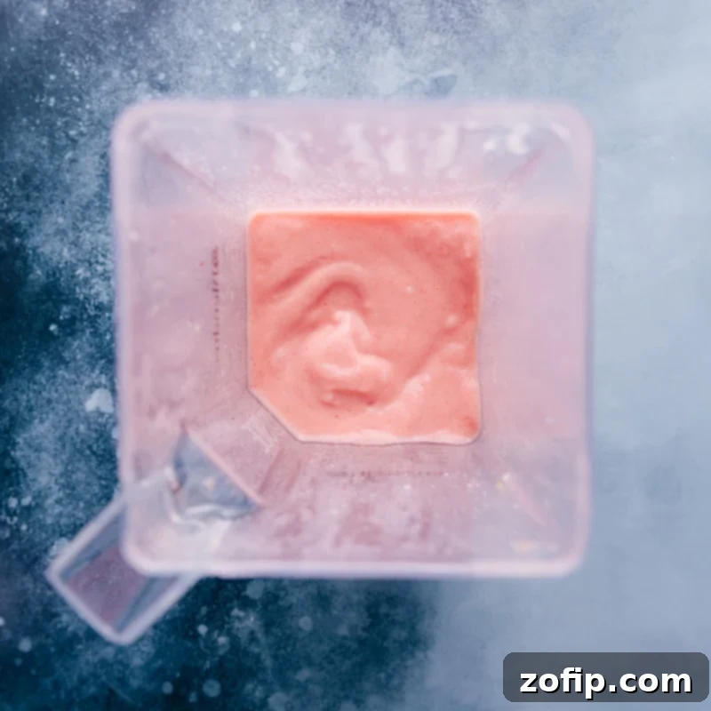 Blending the perfect Strawberry Piña Colada: a close-up of the smooth, creamy mixture in the blender. Overhead close-up shot of a high-powered blender filled with the creamy, pink ingredients of the Strawberry Piña Colada smoothie, mid-blend.