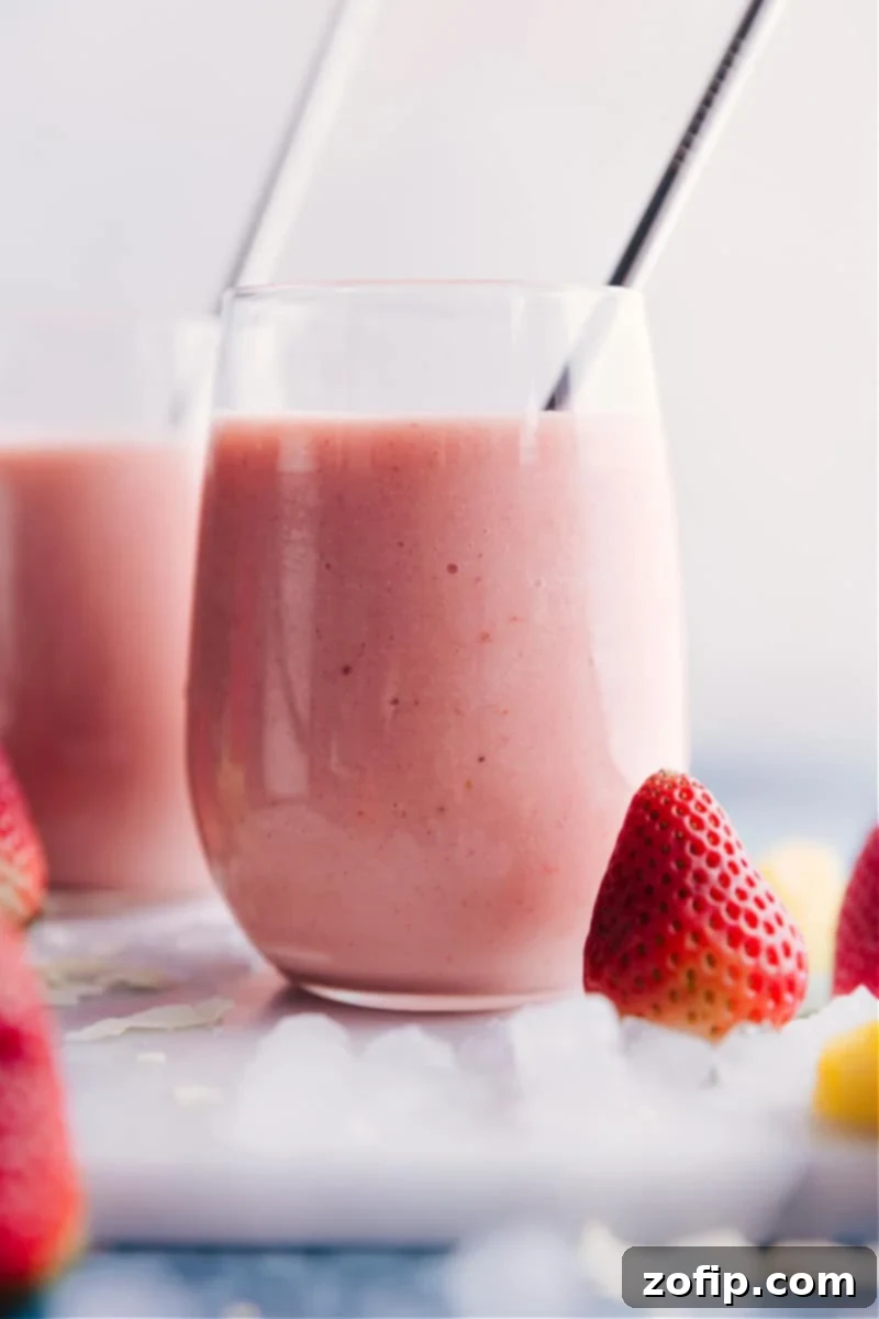 The best ever Strawberry Piña Colada smoothie, ready to enjoy: a creamy, sweet, and tropical delight. A close-up shot of a single Strawberry Piña Colada smoothie in a tall glass, garnished with a fresh strawberry and pineapple, highlighting its creamy texture and vibrant pink color.