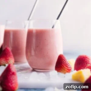 Pink Paradise Colada 2 A single tall glass of Strawberry Piña Colada smoothie, garnished with a fresh strawberry and pineapple wedge, on a wooden table.