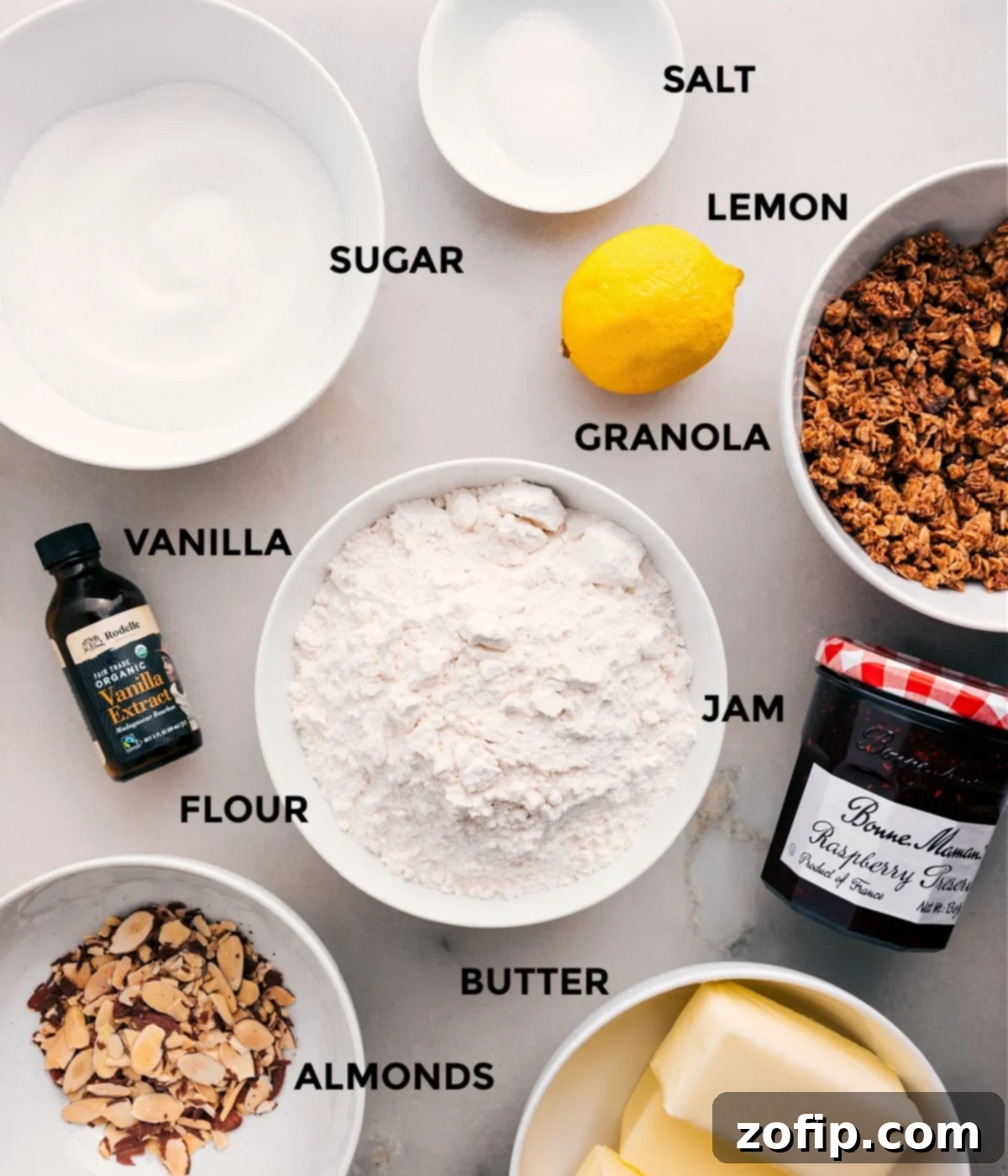 All the essential ingredients for Raspberry Bars prepped and ready: lemon, granola, jam, flour, vanilla, sugar, salt, butter, and almonds.