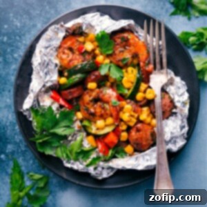 A close-up of a cooked Shrimp Foil Packet, brimming with pink shrimp, sliced sausage, and colorful, tender vegetables.