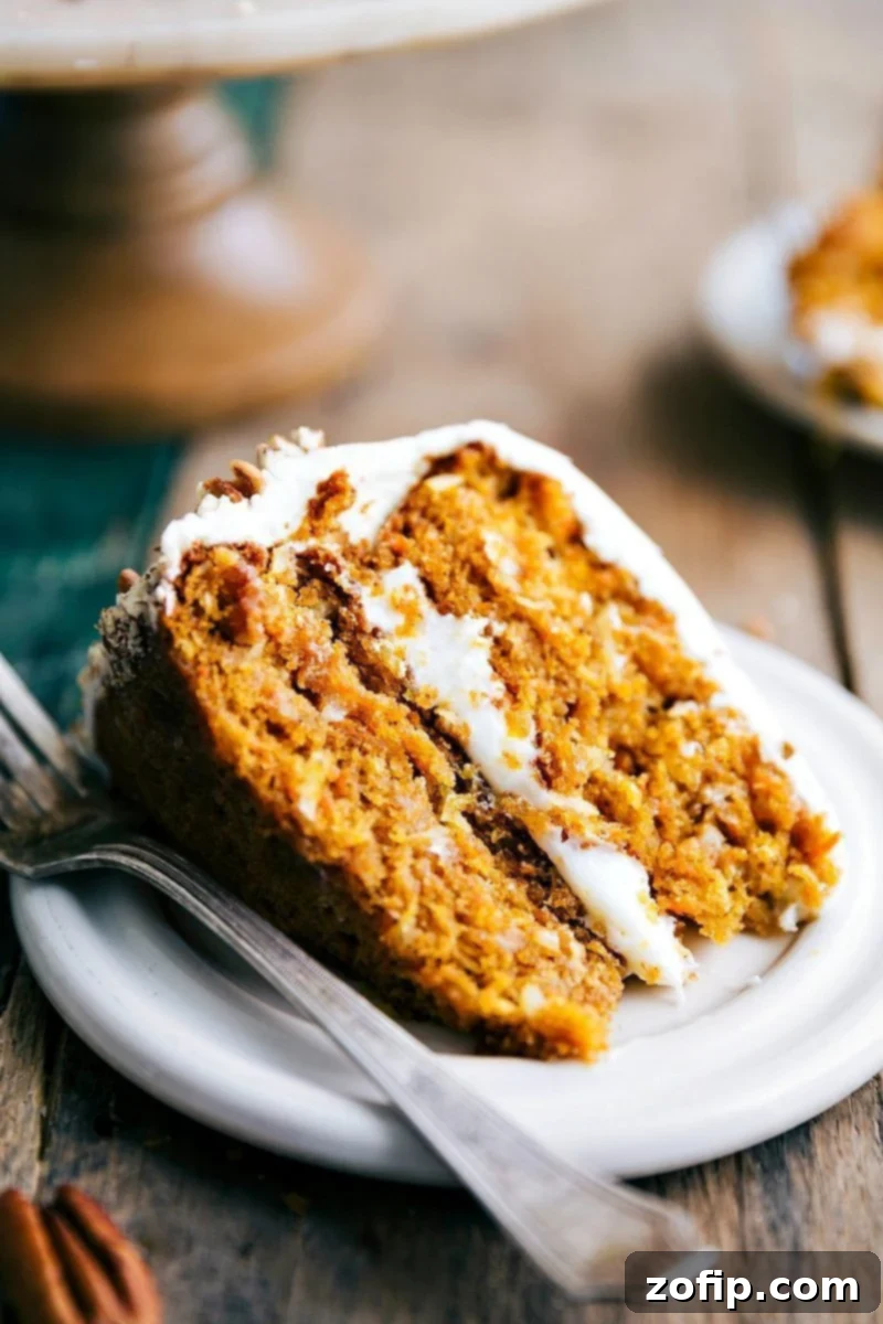 A perfectly sliced piece of moist Pumpkin Carrot Cake, topped with a generous swirl of cream cheese icing, revealing its tender, spiced interior with visible flecks of carrot and pumpkin.