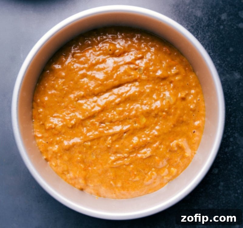 Golden-brown Pumpkin Carrot Cake batter, flecked with carrots and spices, smoothly spread into a parchment-lined round cake pan, ready for baking.