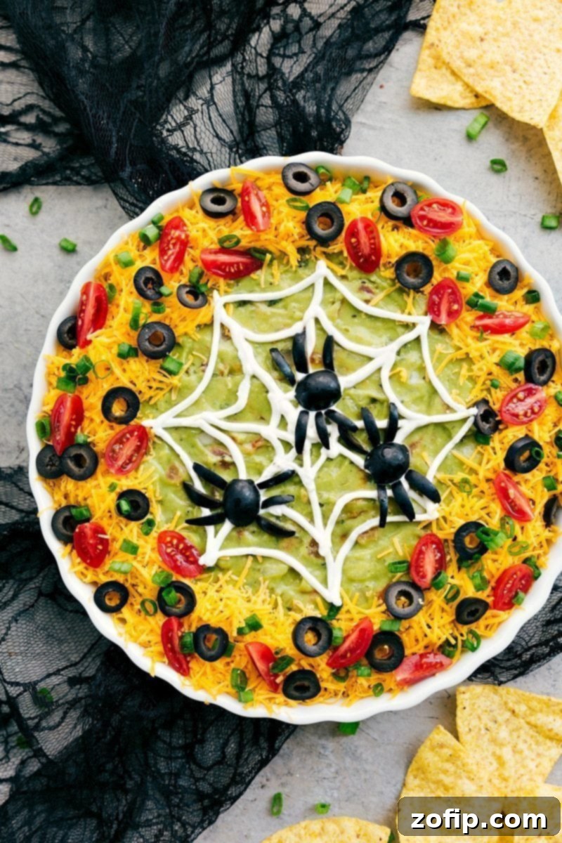 Spider Web: Four easy, & creative Halloween appetizer ideas that are so delicious -- Spider Web 7-Layer Dip, Walking Dead Mummy Dogs, Monster Meatball Sliders, & Cheesy Monster Fingernail Bread. chelseasmessyapron.com #halloween #appetizers #spiderweb #spooky #dip #seven #layer #olives #guacamole Image of a festive spiderweb dip, perfect for easy Halloween appetizers