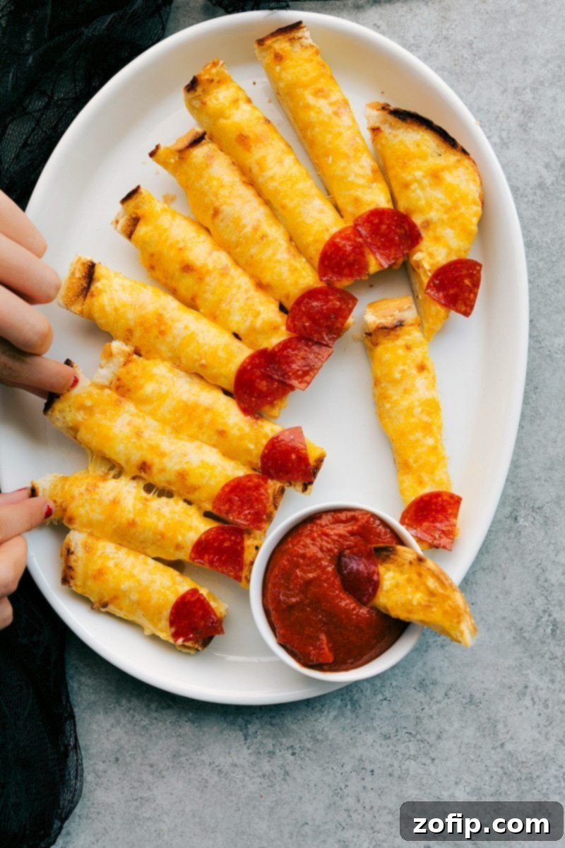 Four easy, & creative best Halloween appetizers that are so delicious -- Spiderweb 7-Layer Dip, Walking Dead Mummy Dogs, Monster Meatball Sliders, & Cheesy Monster Fingernail Bread. chelseasmessyapron.com Image of Cheesy Monster Fingernail Bread, a creative Halloween appetizer with marinara dip