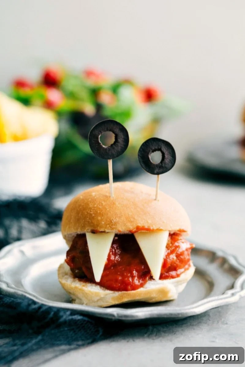 Monster Meatball Sliders: Four easy, & creative Halloween appetizers that are so delicious -- Spiderweb 7-Layer Dip, Walking Dead Mummy Dogs, Monster Meatball Sliders, & Cheesy Monster Fingernail Bread. chelseasmessyapron.com Image of Monster Meatball Sliders with olive eyes and cheese teeth, perfect easy Halloween appetizers