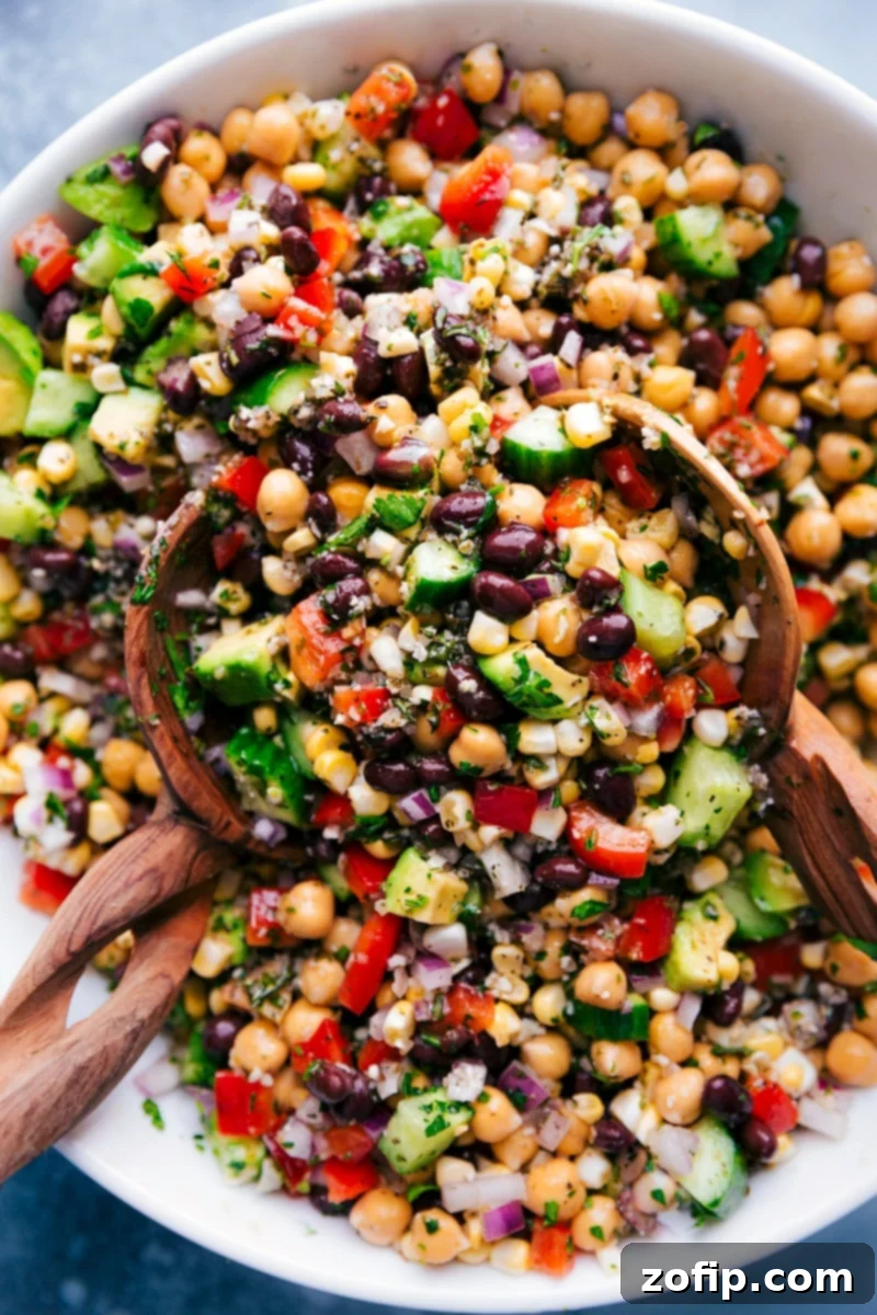 Overhead image of Garbanzo Bean Salad in a bowl with serving spoons, showcasing its colorful ingredients.