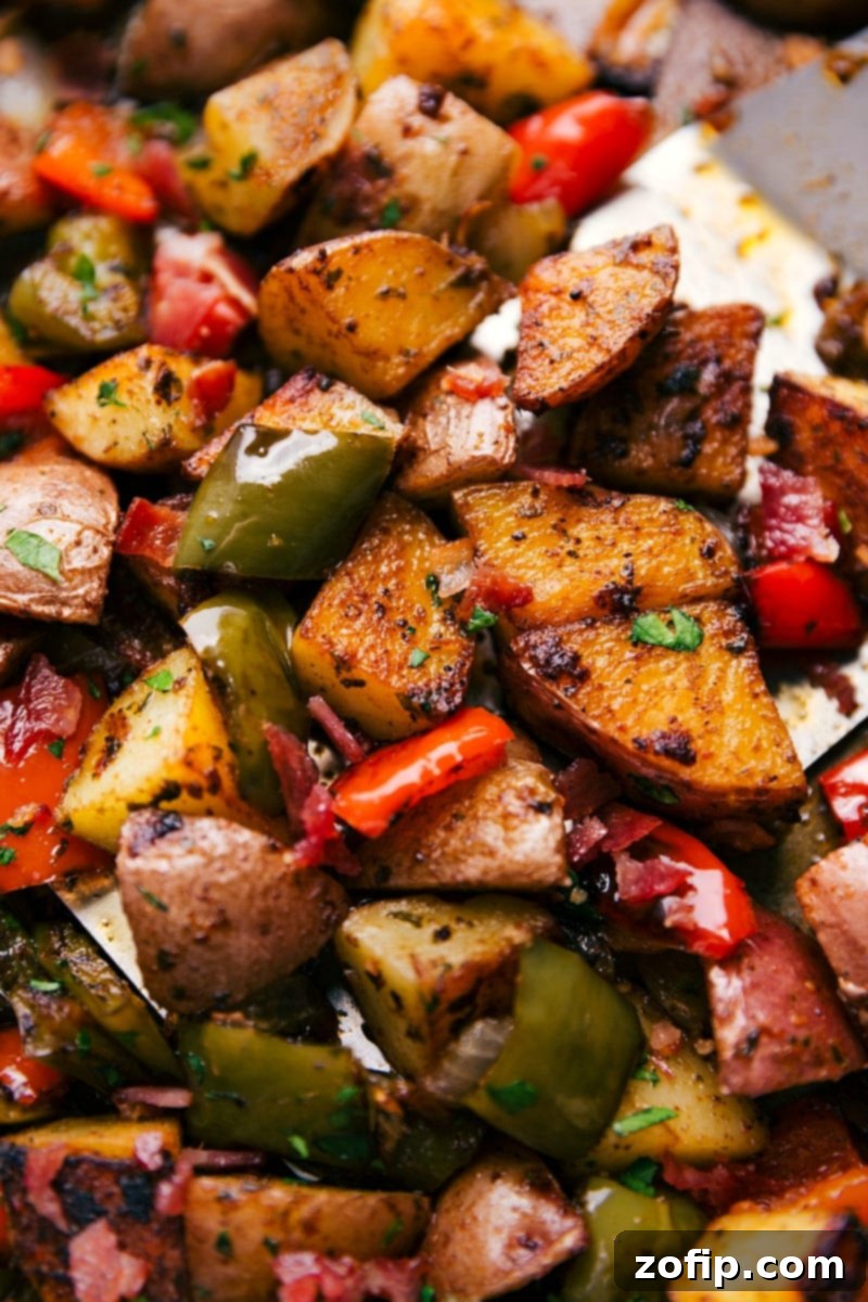 Sheet Pan Bacon Potato Roast 6 A chef's hand tossing diced red potatoes and colorful bell peppers with melted butter and spices on a large sheet pan, ready for roasting.