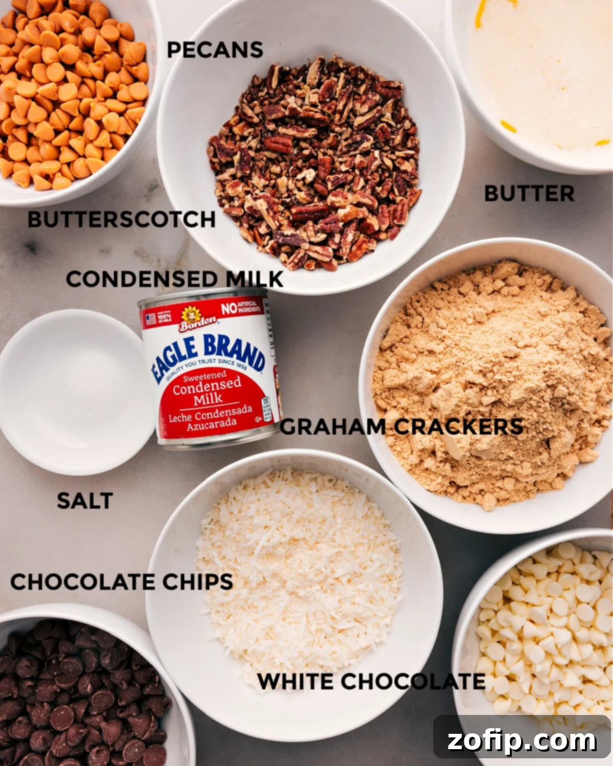 Essential Ingredients for the Best 7-Layer Bars A vibrant display of all the essential ingredients for 7 Layer Bars, including butter, butterscotch chips, pecans, sweetened condensed milk, graham crackers, salt, shredded coconut, and various chocolate chips, ready for assembly.