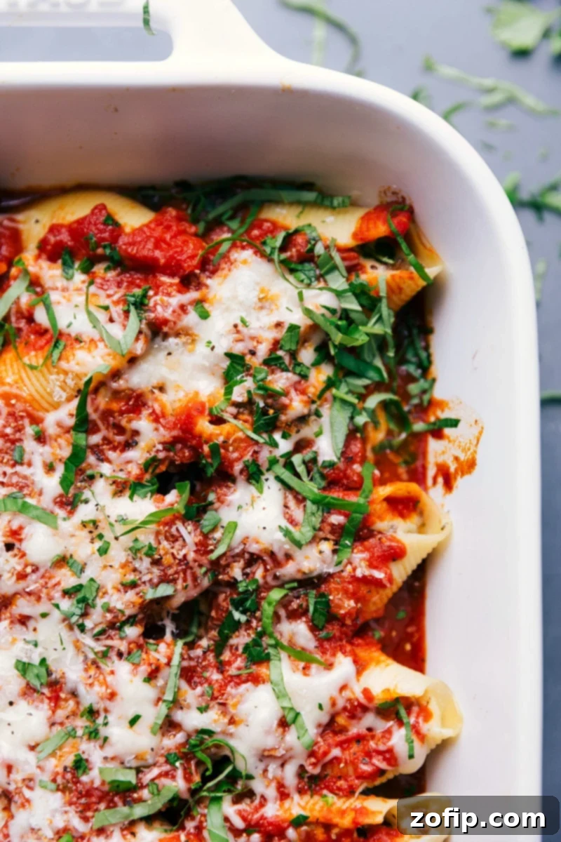 A pan of golden-brown stuffed shells with Italian sausage, generously topped with melted cheese and fresh basil chiffonade, ready to be served as a warm and inviting meal.