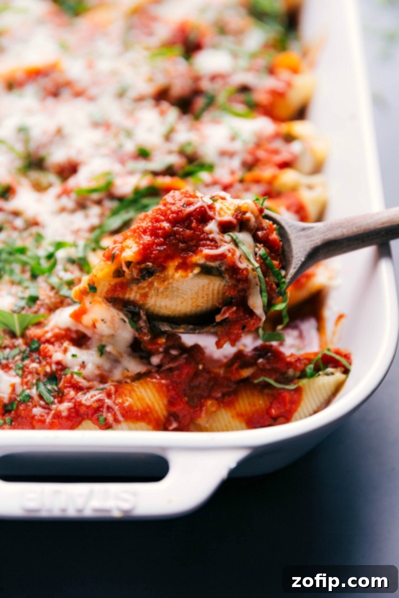 A serving spoon lifting a generous portion of savory stuffed shells with Italian sausage from a baking dish, highlighting the melted cheese and rich filling.