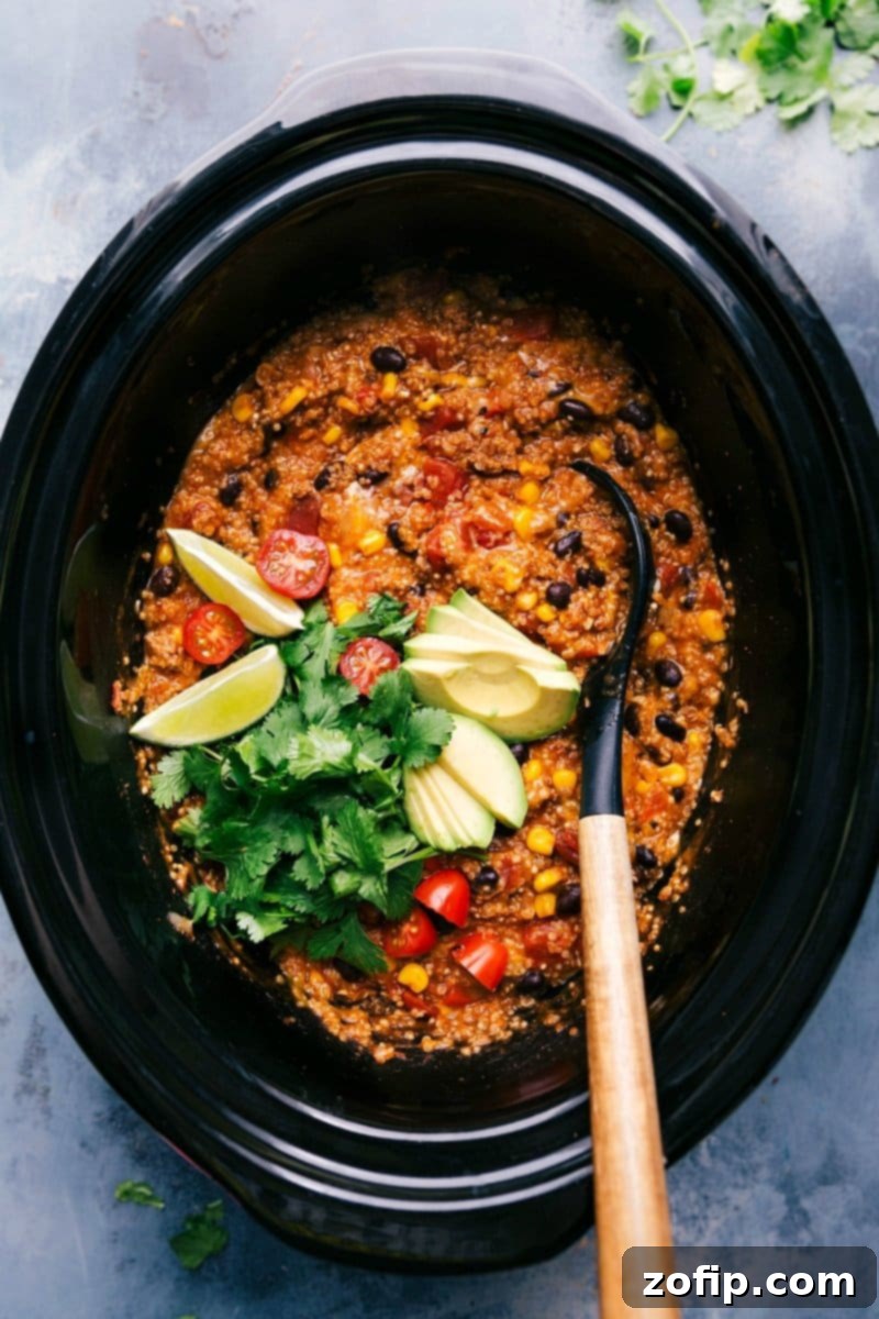 Ready-to-Serve Quinoa Enchilada from Crock-Pot with Fresh Toppings Freshly prepared Quinoa Enchilada Crockpot, served in a rustic bowl with a spoon, generously garnished with vibrant cilantro, diced red tomatoes, sliced avocado, and a refreshing lime wedge, highlighting its readiness to be enjoyed.