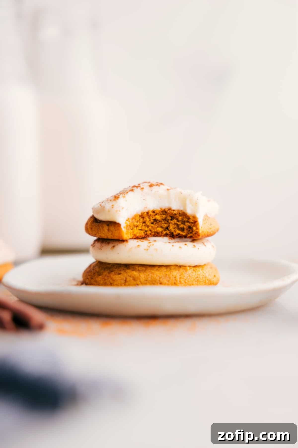 Stack of soft pumpkin cookies with cream cheese frosting on a plate, the top cookie having a bite taken out.