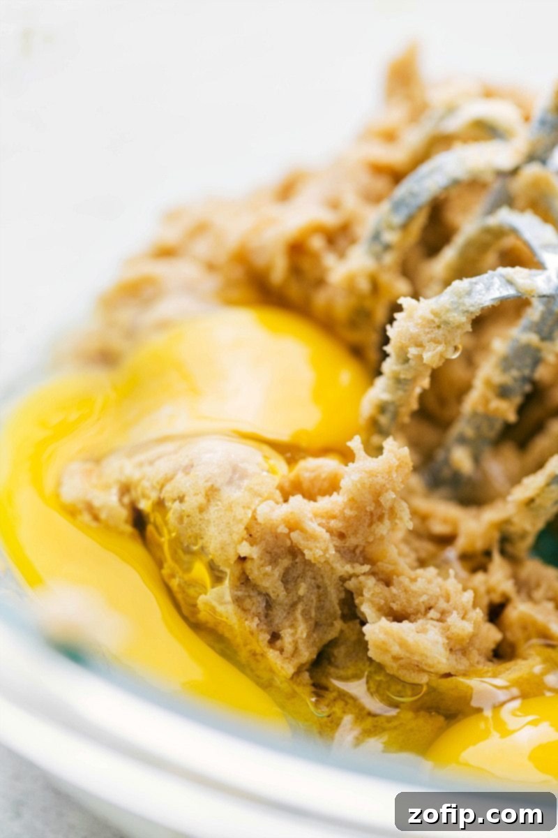 Using an electric hand mixer to combine egg, softened butter, and sugars in a large bowl, creating a smooth and airy mixture for baking.