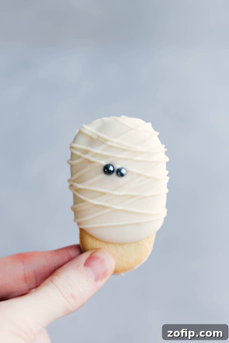 Mummy Milano Cookies - Easy Halloween Treat Idea Delicious Mummy Milano cookies with white chocolate and candy eyes, perfect for Halloween parties.