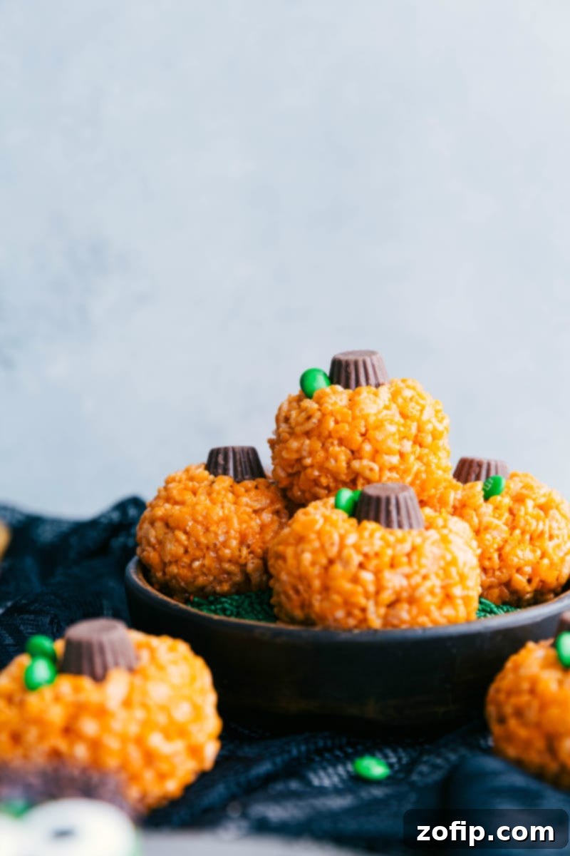 Pumpkin Rice Krispies Treats - Easy Halloween Dessert Ideas Stacked pumpkin Rice Krispies Treats with Reese's cups as stems and green M&M's as leaves.
