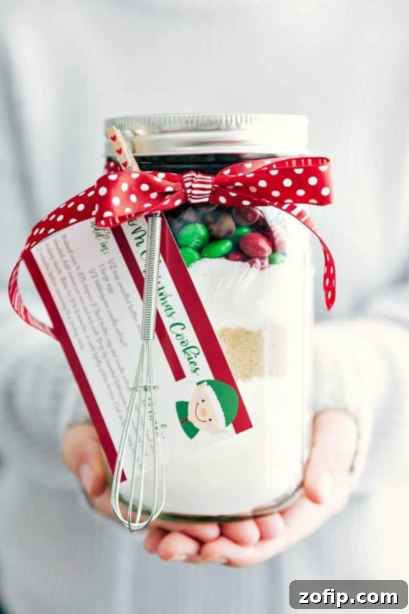Fun And Festive M&M Mason Jar Cookies Gift Beautifully layered M&M Mason Jar Cookies with a festive ribbon and miniature whisk, ready to be gifted for Christmas.