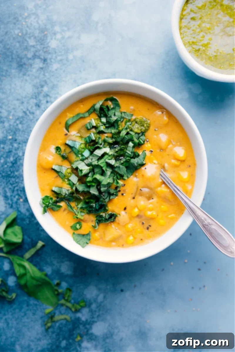 Delicious and creamy Potato Corn Chowder garnished with fresh basil and a swirl of pesto, served in a rustic bowl.