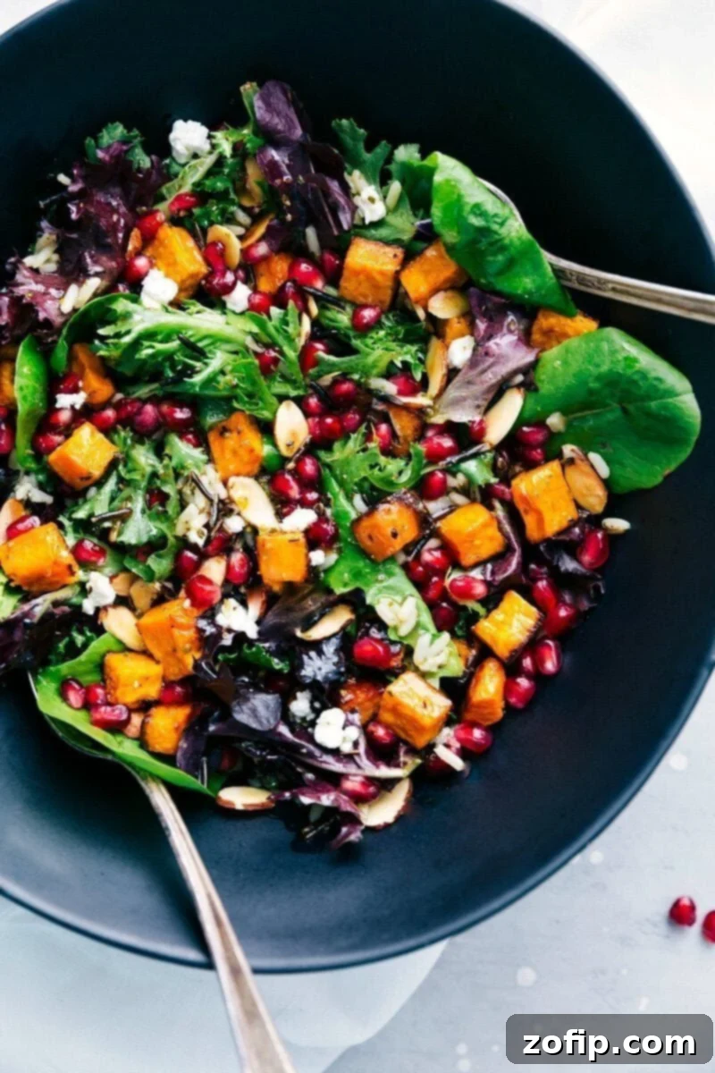 Overhead image of a vibrant Wild Rice Salad in a large serving bowl, showcasing mixed greens, roasted sweet potatoes, pomegranate seeds, feta cheese, and almonds.