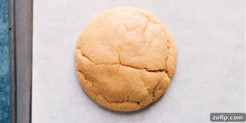 Overhead shot of a freshly baked, warm, and perfectly golden peanut butter cookie, highlighting its thick, soft texture.