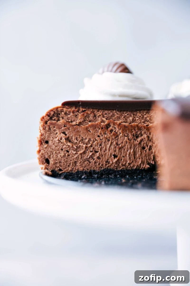 A perfectly sliced chocolate cheesecake with a rich ganache topping and an Oreo cookie crust, sitting on a white plate, ready to be enjoyed.