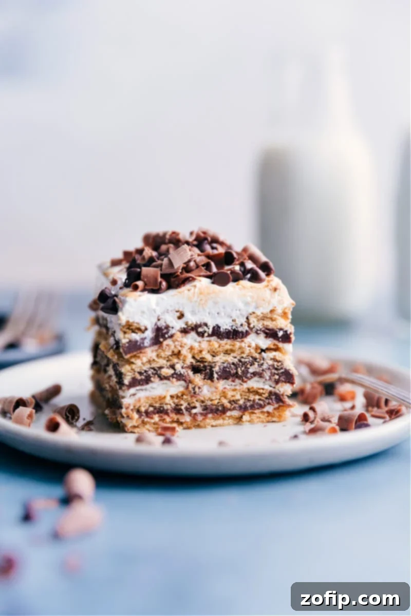 This S'mores Icebox Cake features layers of rich chocolate ganache, fluffy marshmallow cream, and honey graham crackers. No baking required! Recipe via ChelseasMessyApron #dessert #best #quick #easy #simple #treat #chocolate #marshamallow #grahamcrackers #summer #smores #icebox #cake A beautifully layered S'mores Icebox Cake on a plate, showcasing rich chocolate, white marshmallow, and graham cracker layers, ready to be enjoyed.