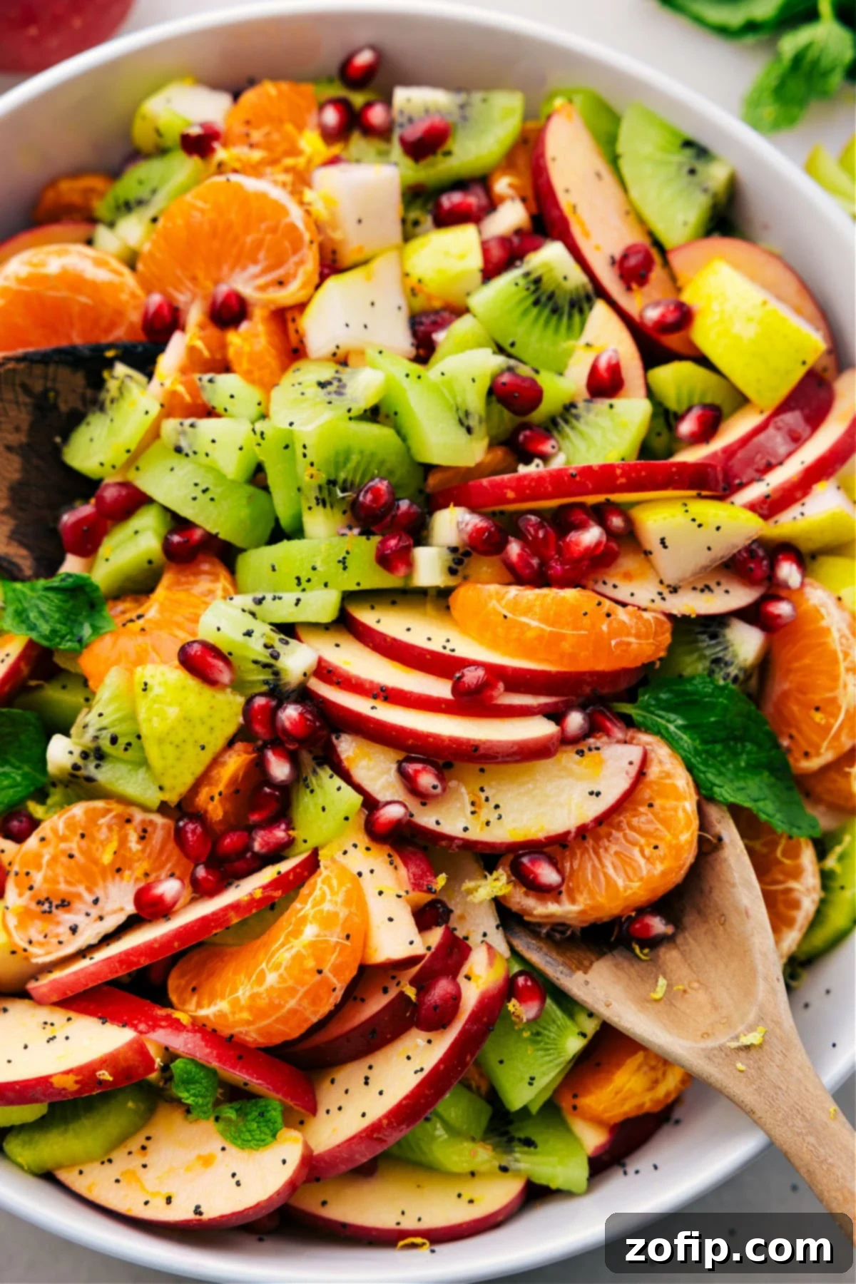 A vibrant bowl of Winter Fruit Salad featuring clementines, pomegranate, apples, kiwi, and pears, perfectly dressed and ready to be enjoyed.