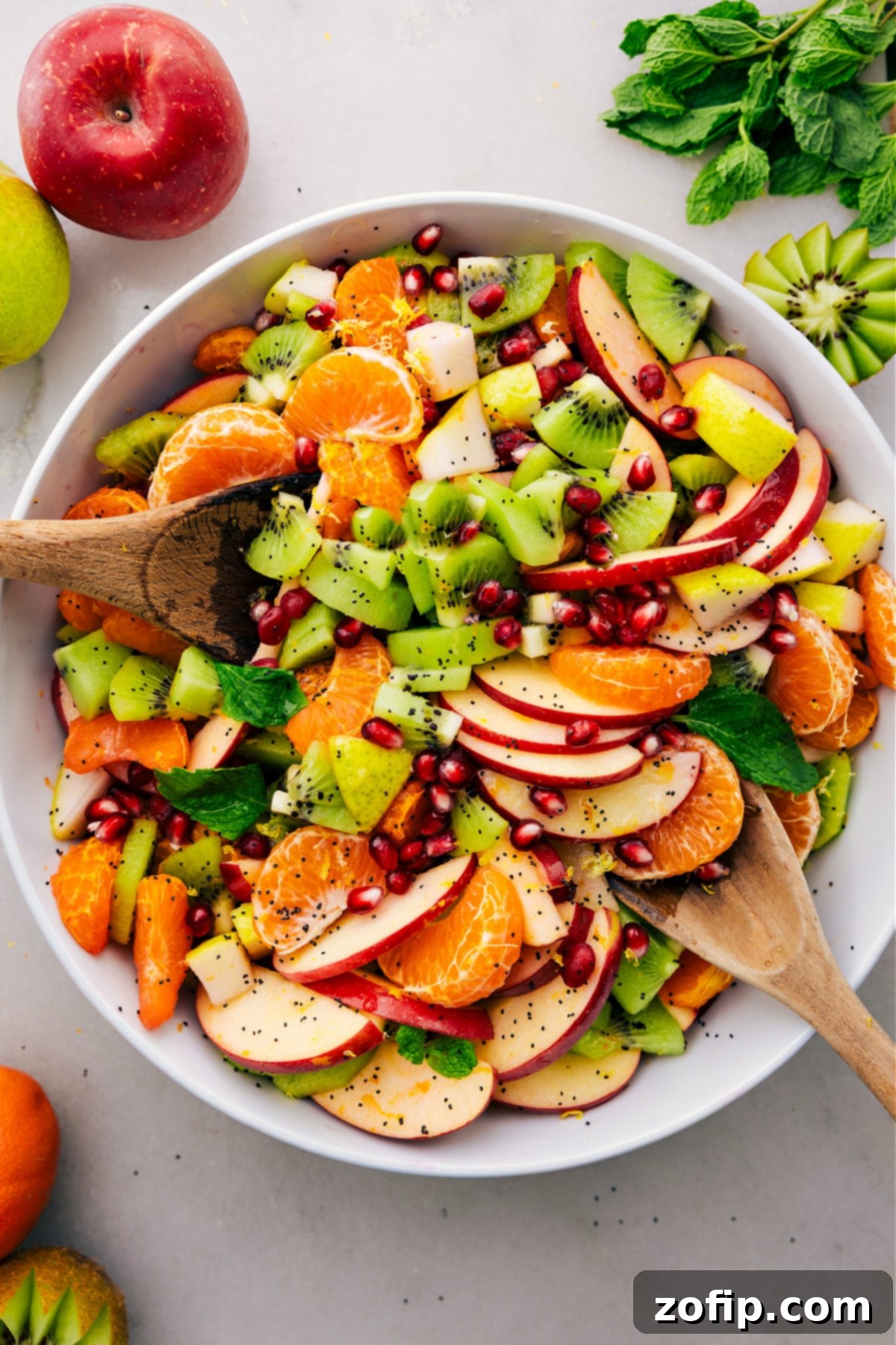 A close-up of a fresh and delicious winter fruit salad, glistening with dressing and topped with pomegranate seeds, served in an elegant bowl.