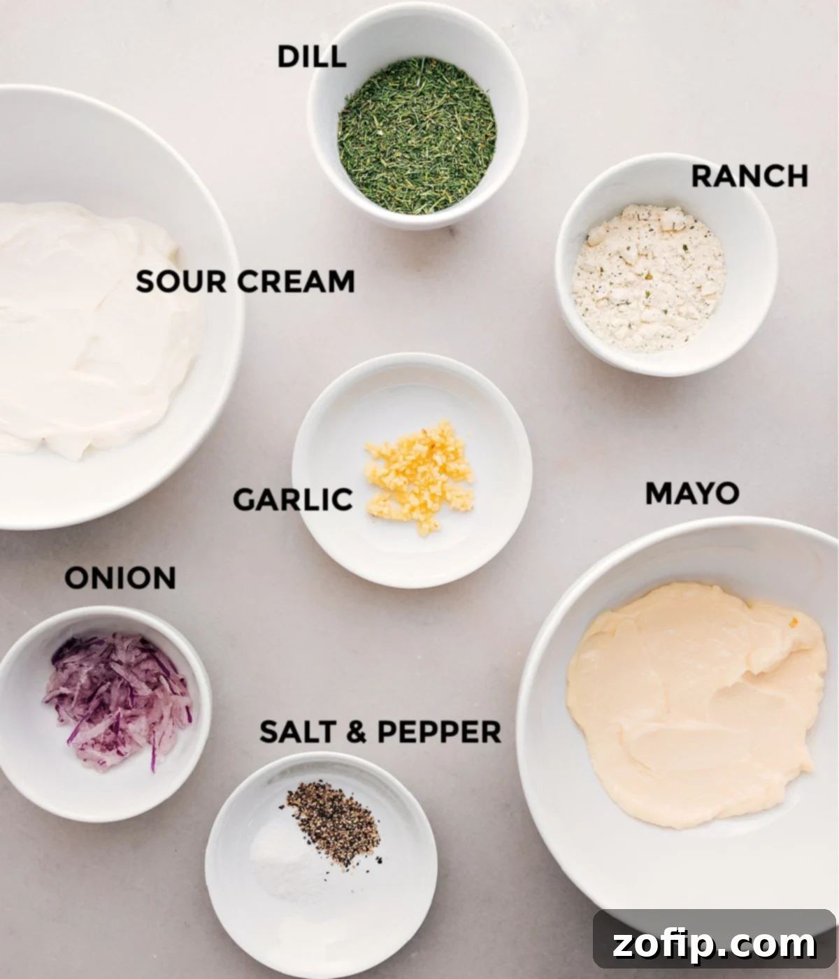A collection of fresh, high-quality ingredients laid out on a clean surface, including a bowl of sour cream, a jar of mayonnaise, a packet of ranch seasoning, fresh dill, minced garlic, grated red onion, salt, and pepper – all essential for making the best veggie dip.