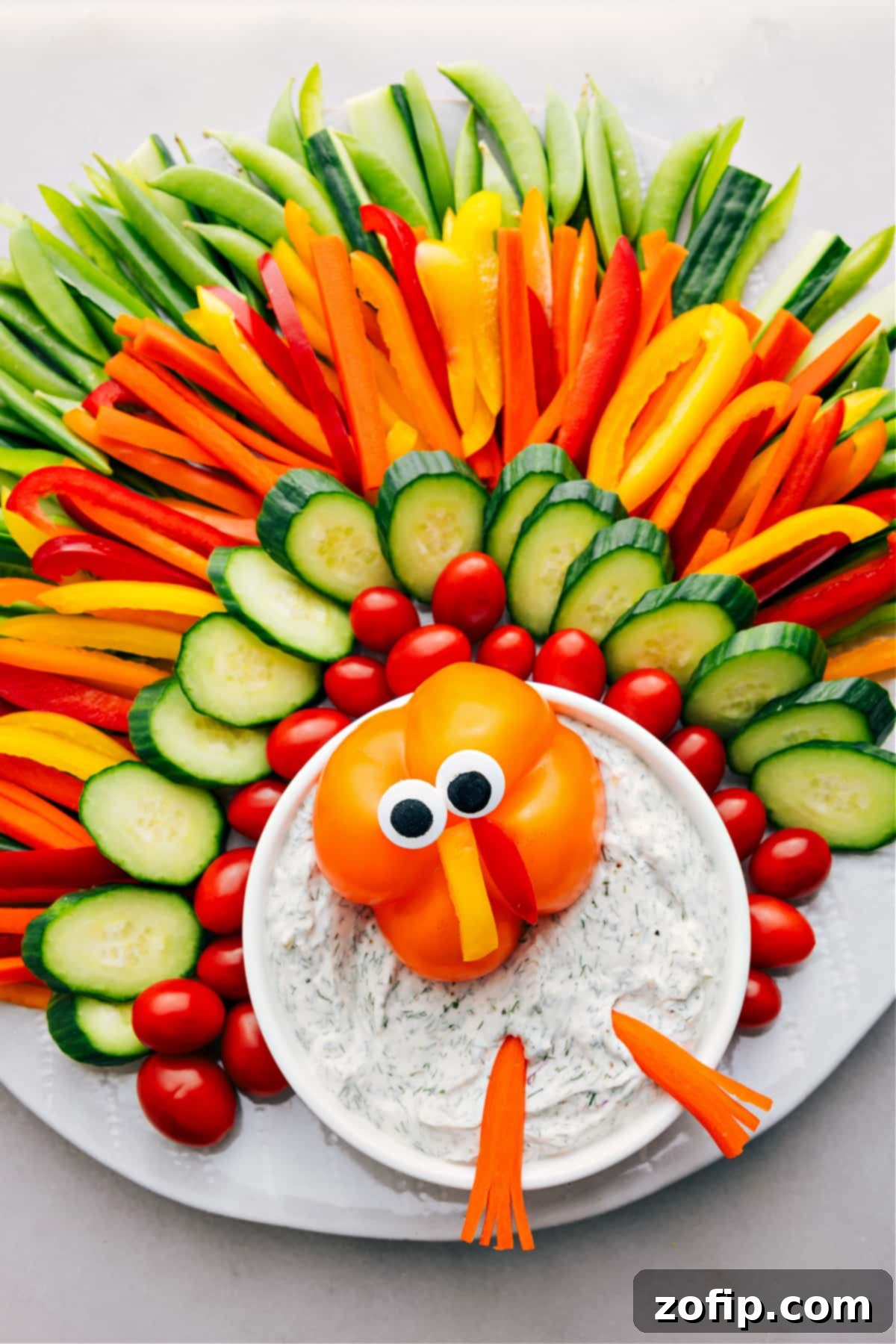 A festive Thanksgiving appetizer featuring fresh vegetables artfully arranged to resemble a turkey, served with a bowl of delicious veggie dip.