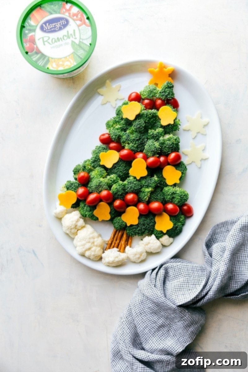A cheerful Christmas tree-shaped arrangement of fresh vegetables, served with a bowl of homemade veggie dip, making a festive and healthy holiday snack.