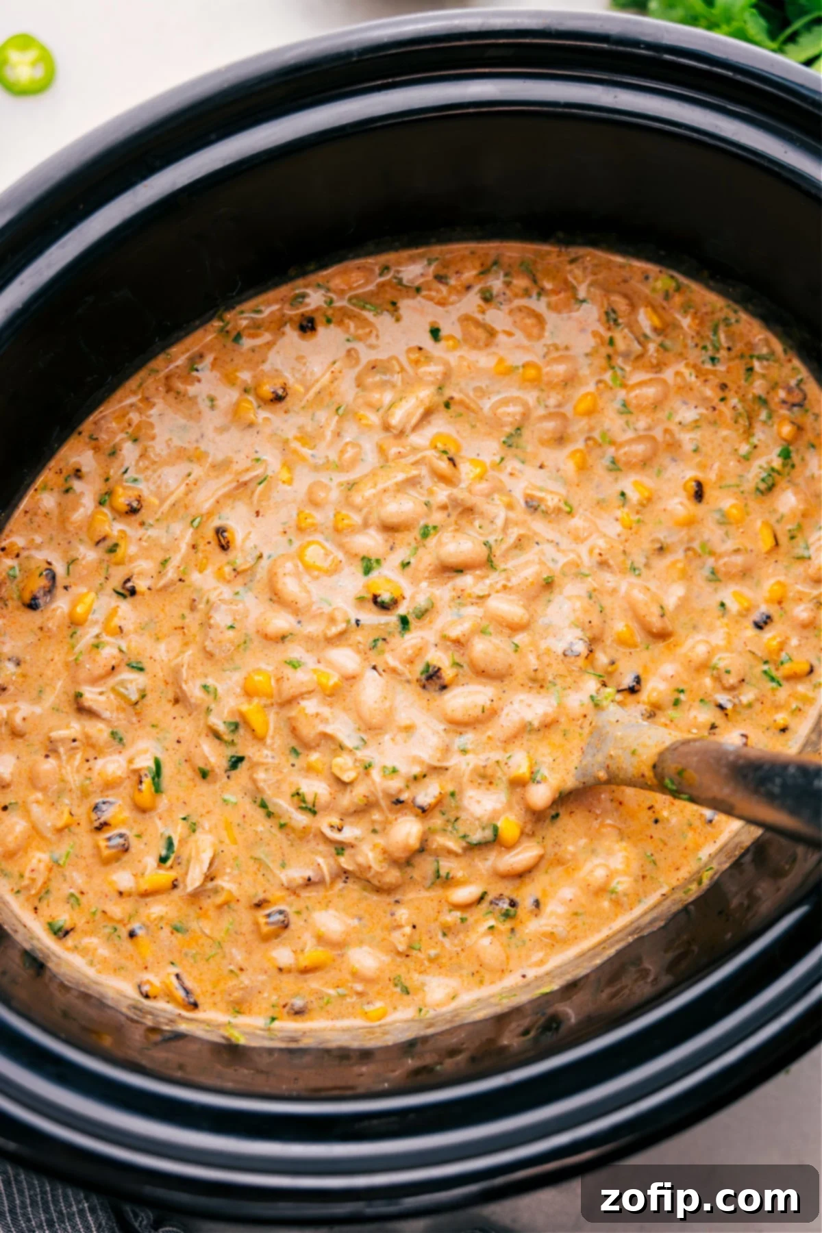 The Best Crockpot White Chicken Chili Recipe A slow cooker filled with creamy Crockpot White Chicken Chili, showcasing chicken, beans, and corn.