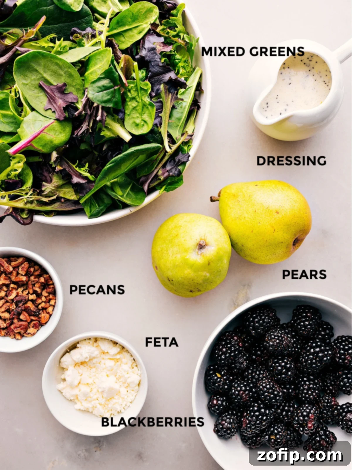 All the fresh ingredients for this delicious Blackberry Salad, including a vibrant spring mix, plump blackberries, sliced pears, crumbled feta, and candied pecans, neatly prepped for assembly.
