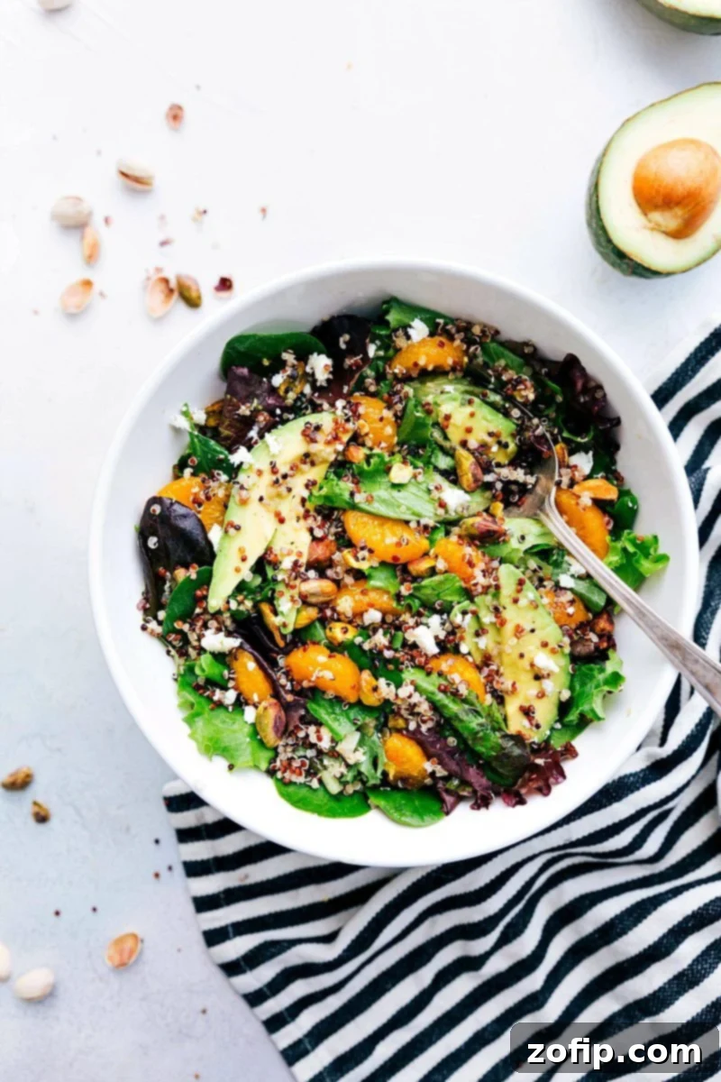 Overhead shot of a beautifully arranged Citrus Quinoa Salad bowl, showcasing the vibrant colors of clementines, green pistachios, and fresh mixed greens.