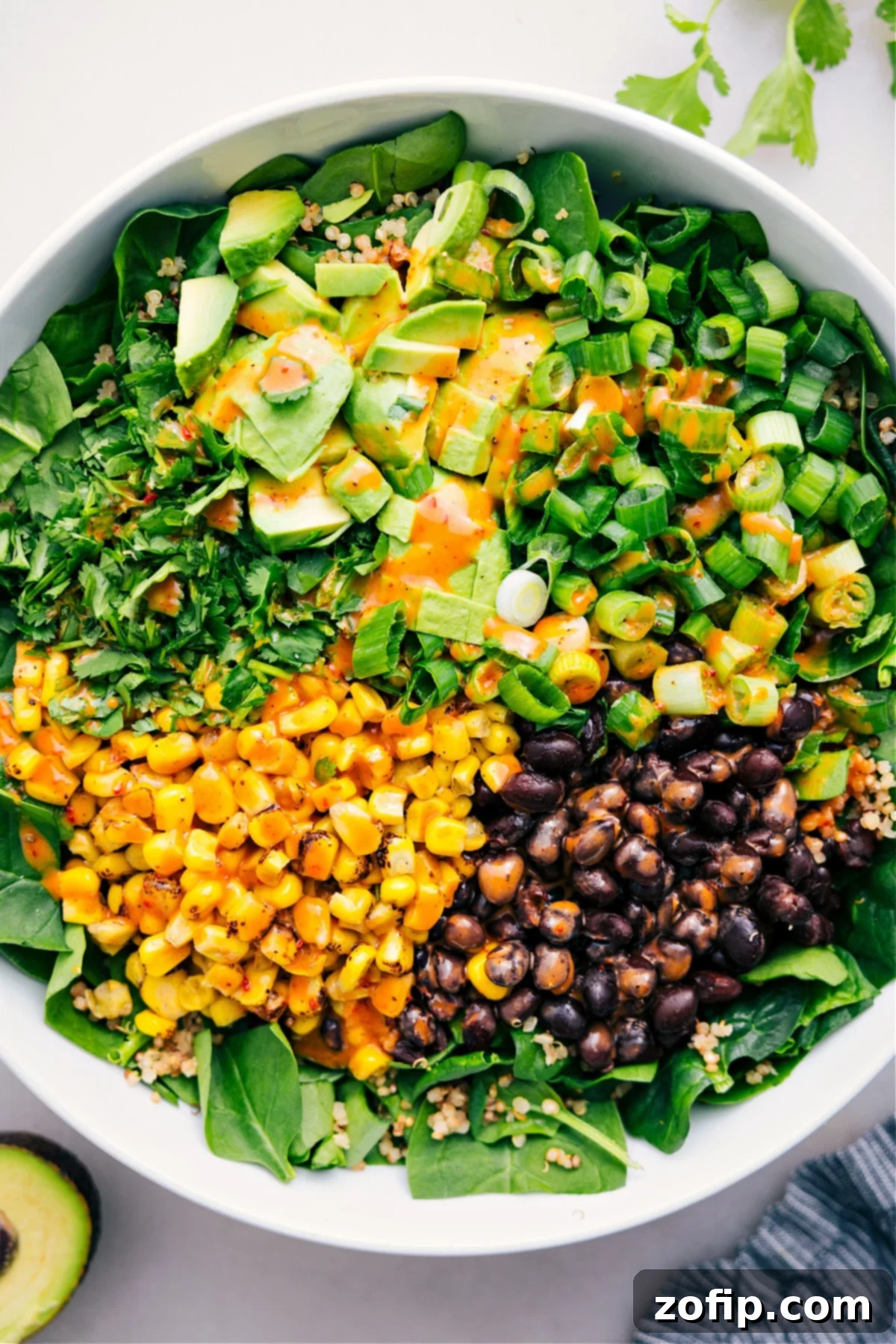 A vibrant bowl of Quinoa Corn Salad, featuring fluffy quinoa, yellow corn kernels, black beans, diced avocado, and fresh cilantro, with a rich chipotle-lime dressing drizzled over it.