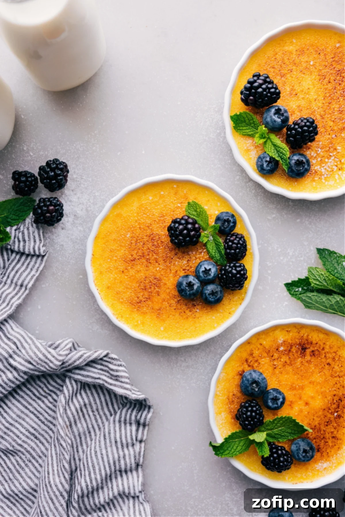 Golden crème brûlées with a crisp sugary top, beautifully garnished with fresh berries and mint leaves, ready to be served.