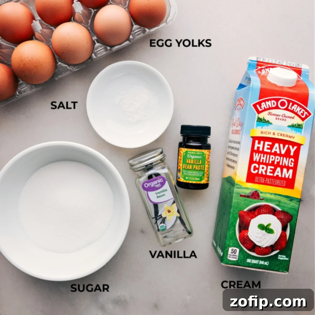 A beautiful flat lay of fresh ingredients for Crème Brûlée, including golden egg yolks, a fragrant vanilla bean, a measuring cup of heavy cream, and sugar, all meticulously arranged on a rustic wooden board.