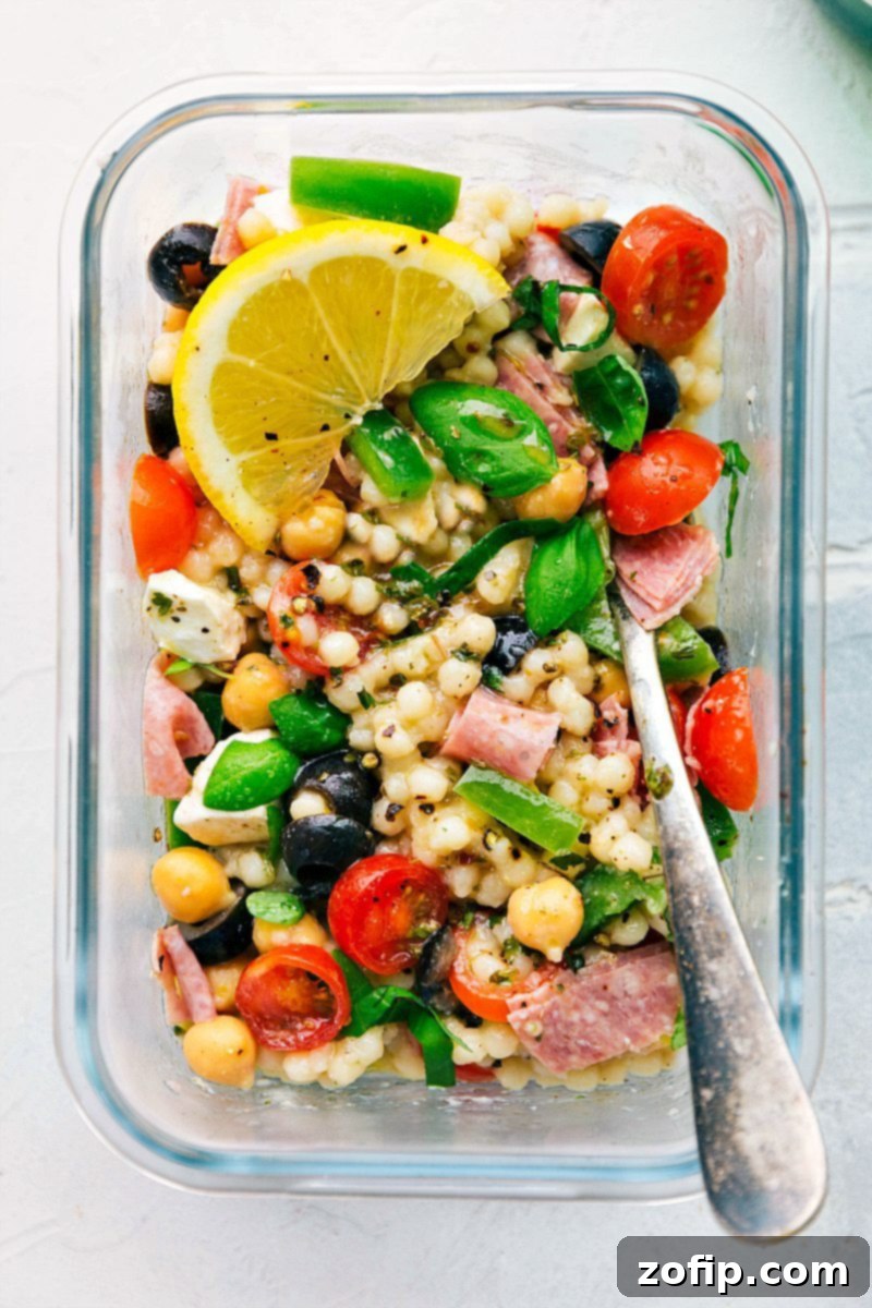 Meal Prep Italian Couscous Salad 5 Overhead shot of six individual meal prep containers filled with Italian Couscous Salad, each with a separate dressing container and a lemon wedge, showcasing organized healthy eating.