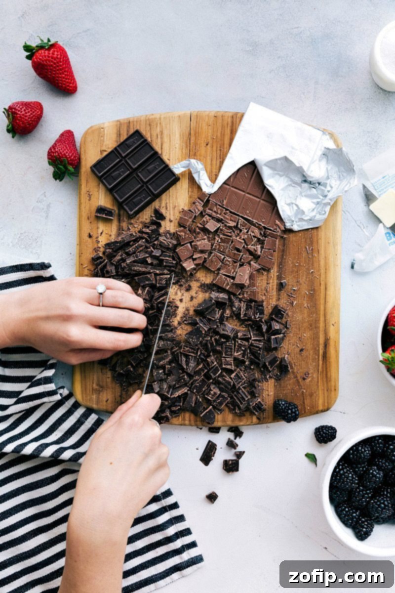 Two different types of chocolate, semi-sweet and milk chocolate, being chopped into small pieces, ready to be melted for the fondue recipe.