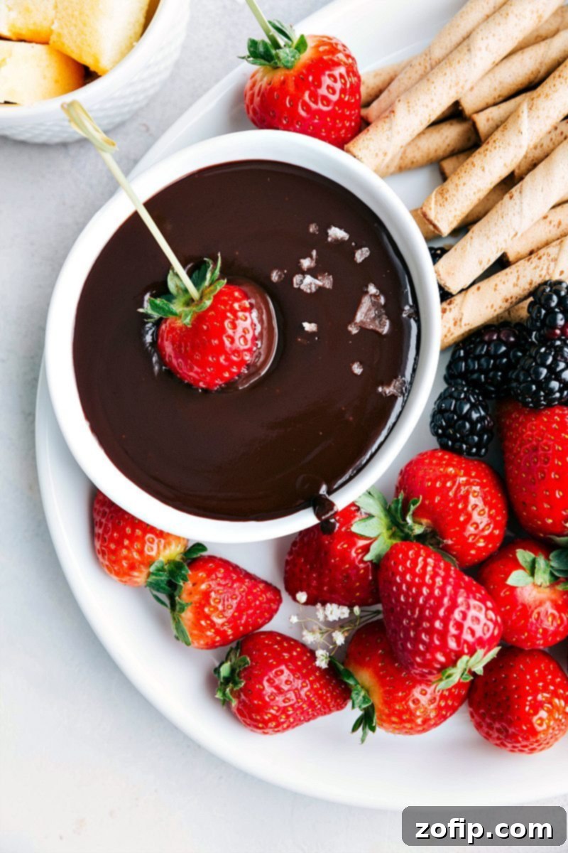 A selection of fruits and cookies arranged around a bowl of chocolate fondue, ready for dipping.