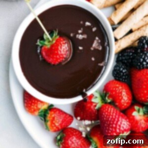 A top-down view of a bowl of chocolate fondue with various dippers like strawberries and cookies.